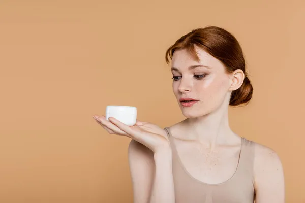 Young Redhead Woman Looking Jar Cosmetic Cream Isolated Beige — Stock Photo, Image