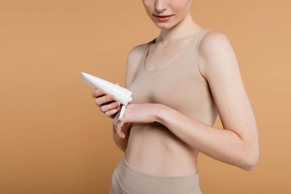 ベージュに隔離された化粧水と泡の保持チューブを持つ若い女性のクロップビュー — ストック写真