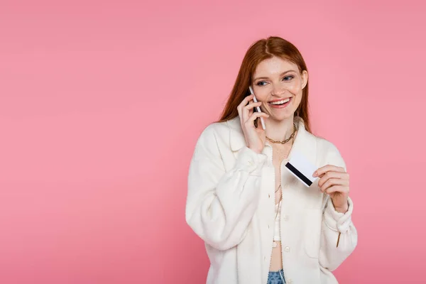 一个时髦的雀斑女人用智能手机说话 手里拿着用粉红隔开的信用卡 — 图库照片