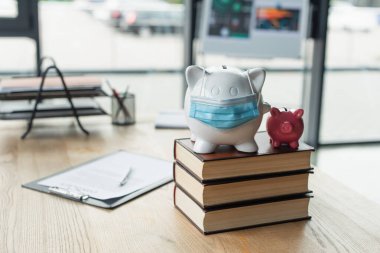 piggy banks with medical mask on codex books near blurred contract on desk, anti-corruption concept clipart