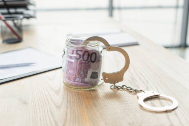 Avro banknotları ve bulanık belgenin yanında kelepçe bulunan cam kavanoz, yolsuzlukla mücadele kavramı