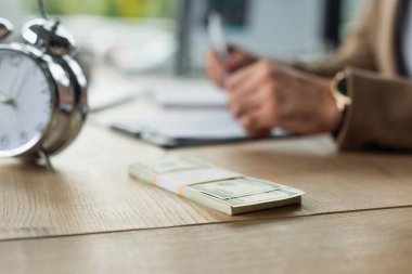 Çalar saatin yanındaki dolar banknotları ve bulanık arka plan ve yolsuzlukla mücadele konsepti üzerine kesilmiş iş adamları.