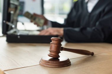 Tahta tokmağın seçici odak noktası kırpılmış yargıç ve para dolu evrak çantası bulanık arka plan, yolsuzlukla mücadele konsepti