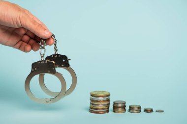 Mavi, yolsuzlukla mücadele konsepti üzerinde gümüş ve altın para yığınlarının yanında kelepçe tutan adamın kısmi görüşü