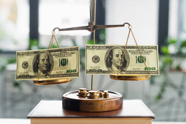 KYIV, UKRAINE - SEPTEMBER 22, 2021: bronze justice scales with dollar banknotes on codex book in office, anti-corruption concept