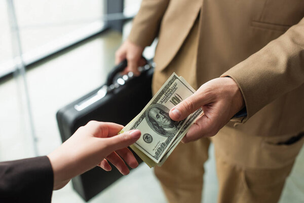 КИЕВ, УКРАИНА - 22 СЕНТЯБРЯ 2021: частичный взгляд бизнесмена с размытым портфелем, дающим деньги женщине, антикоррупционная концепция