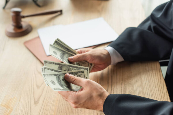 cropped view of judge counting dollar banknotes near papers and gavel, anti-corruption concept