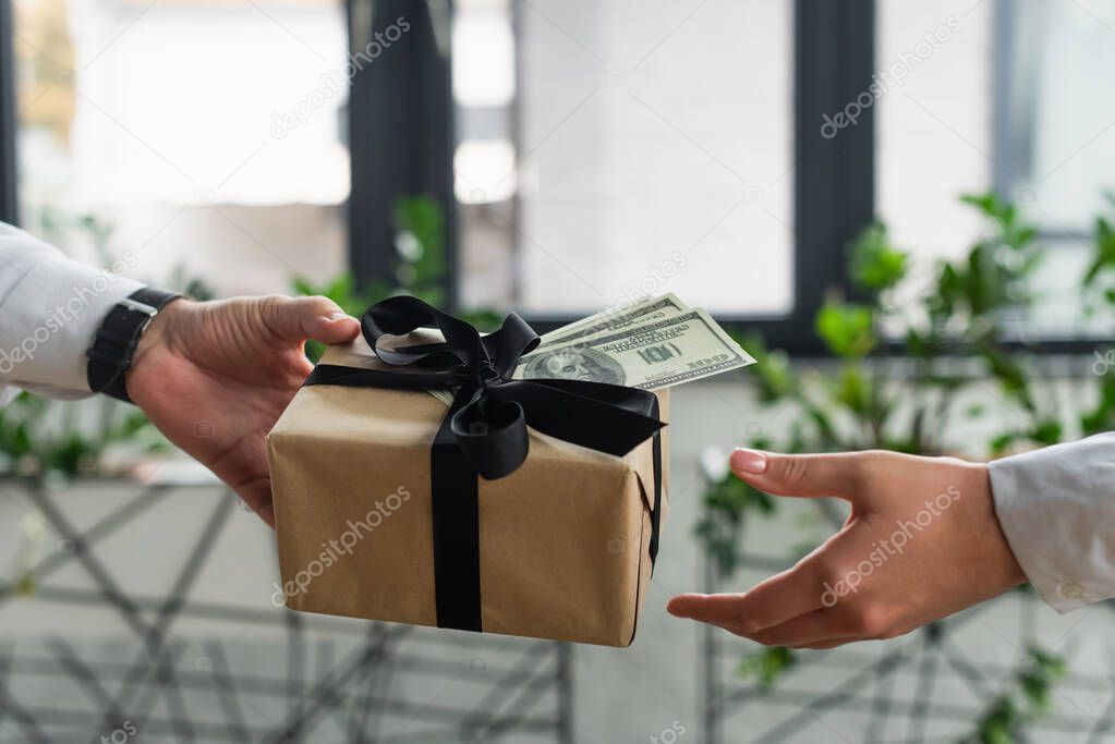 partial view of businessman giving present and money to woman in office, anti-corruption concept