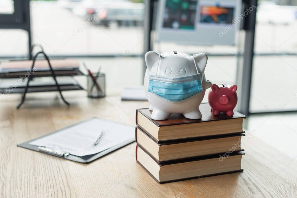 piggy banks with medical mask on codex books near blurred contract on desk, anti-corruption concept