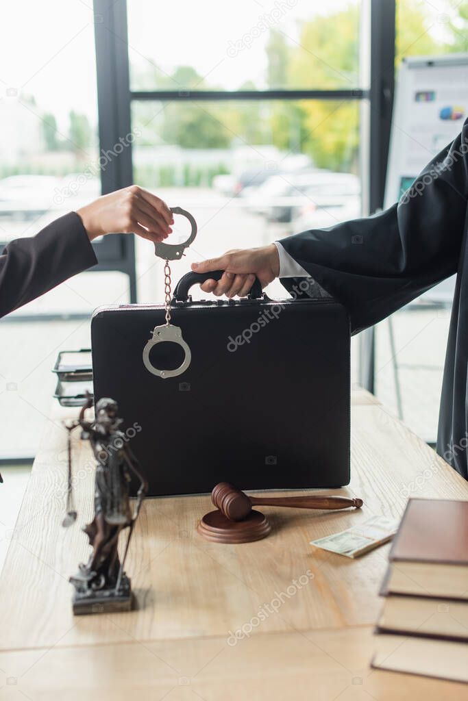 cropped view of woman holding handcuffs near judge with briefcase, anti-corruption concept