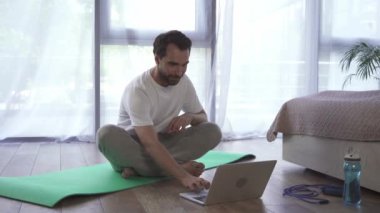 Evde meditasyon yaparken dizüstü bilgisayar kullanan bir adam. 