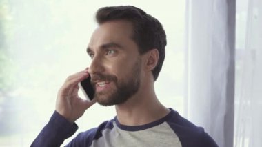 Evde cep telefonuyla konuşan pozitif sakallı adam. 