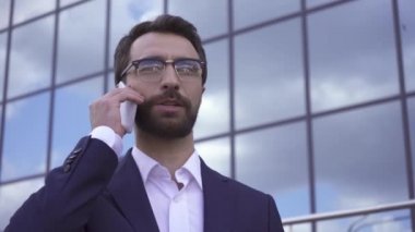 Gülümseyen işadamı dışarıda akıllı telefondan konuşuyor. 