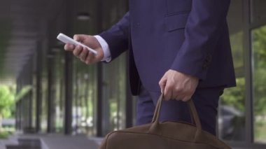 Açık havada akıllı telefon kullanan çantalı iş adamının görüntüsü. 