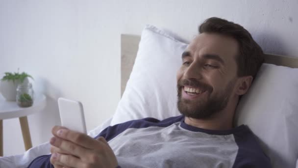 Fröhlicher Mann Benutzt Handy Während Hause Bett Liegt — Stockvideo