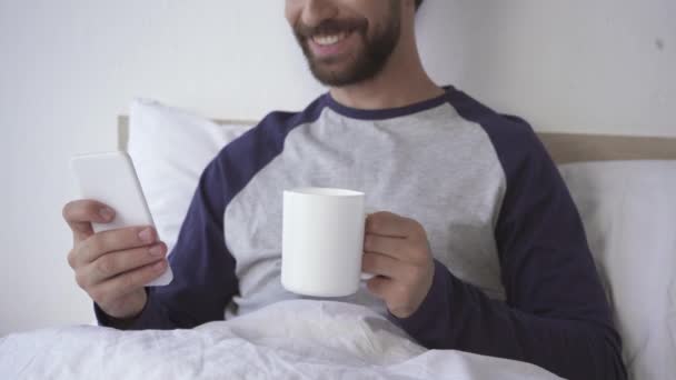 Vista Cortada Homem Sorridente Com Café Usando Celular Cama — Vídeo de Stock