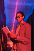 african american programmer looking at digital tablet while working in data center in neon light