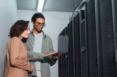 Afrikalı Amerikalı programcı veri merkezinde çalışırken bilgisayarını meslektaşına gösteriyor.