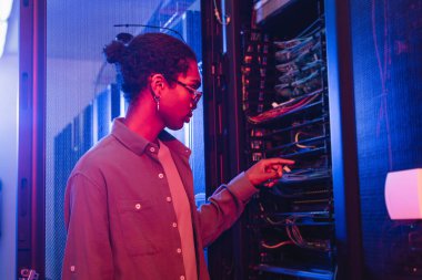 Afrikalı Amerikalı teknisyen veri merkezindeki sunucu kablolarını kontrol ediyor.