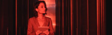 Dijital tabletli genç bir kadın veri merkezindeki sunuculara neon ışığı ve pankartıyla bakıyor