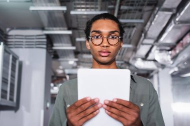 Veri merkezindeki kameraya bakarken dijital tablet tutan genç Afrikalı Amerikalı programcı