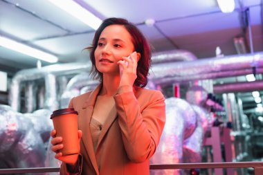 Veri merkezinin teknik ekipman odasında cep telefonuyla konuşmak için kahve getiren genç mühendis.