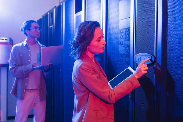 молодой инженер с цифровым сервером проверки планшета рядом с африканским американским коллегой с ноутбуком