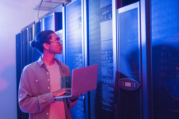 african american programmer with digital tablet working in data center in neon light