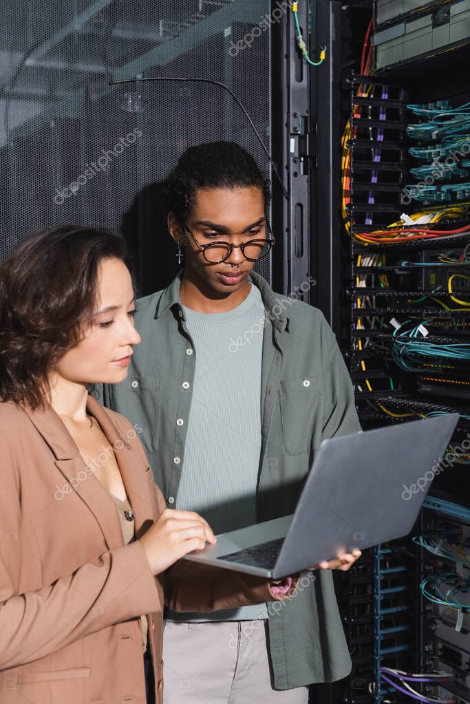 Multiethnic technicians working on laptop near server in data center