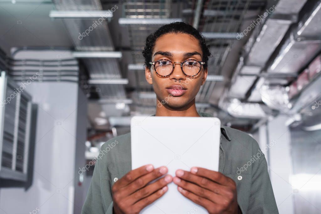 Young african american programmer holding digital tablet while looking at camera in data center