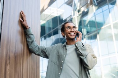 Mutlu ve şık Afro-Amerikan adam dışarıda cep telefonuyla konuşuyor.