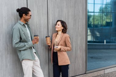 Kahveli pozitif ırklar arası arkadaşlar dışarıda gri duvarın yanında konuşuyorlar.