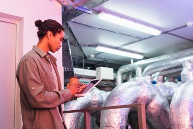 Afgan Amerikan mühendisi dijital tablet ve kahveyle veri merkezinin teknik ekipman odasında çalışacak.