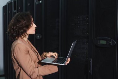 programmer using laptop while checking servers in data center clipart