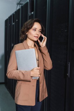 Veri merkezinde çalışırken cep telefonuyla konuşan dizüstü bilgisayarı olan teknisyen