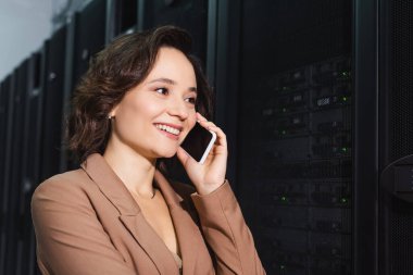 happy engineer talking on mobile phone near servers in data center clipart