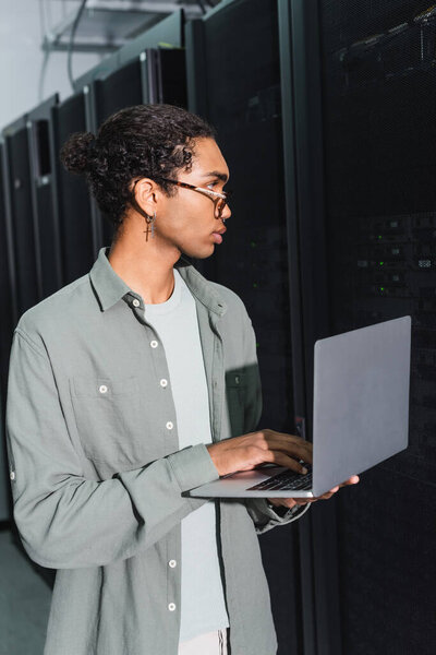 young african american programmer using laptop while working with servers in data center