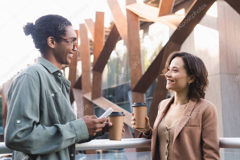 smiling african american man with smartphone talking with young woman outdoors