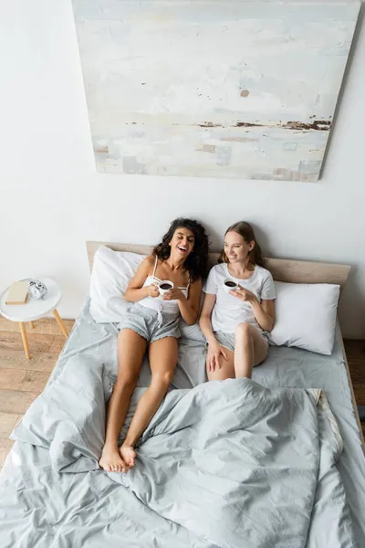 幸せなレズビアンカップルがベッドでコーヒーを飲みながら — ストック写真