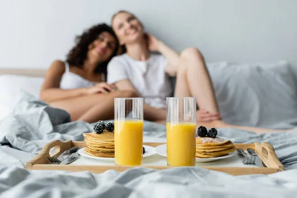 带橙汁的玻璃杯和盘子里的煎饼接近模糊的女同性恋夫妇 — 图库照片