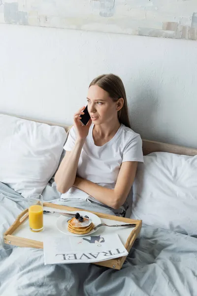 Mujer Joven Hablando Teléfono Inteligente Cerca Bandeja Con Desayuno Dormitorio — Foto de Stock