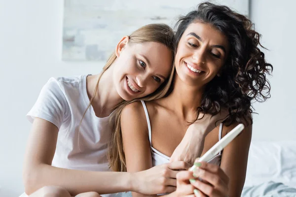 Cheerful Woman Holding Pregnancy Test While Hugging Happy Girlfriend Bedroom — Stock Photo, Image