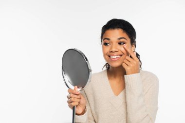 Kontakt lens takan ve elinde beyaz bir ayna tutan Afro-Amerikan kadın.