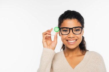 Smiling african american woman in eyeglasses holding contact lenses and looking at camera isolated on white clipart