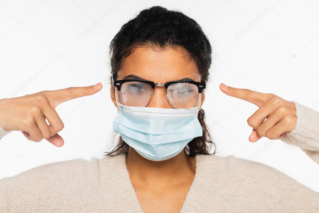 African american woman in medical mask pointing at fogged eyeglasses isolated on white