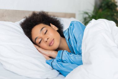 Kıvırcık Afrikalı Amerikalı kadın yatak odasında uyuyor. 