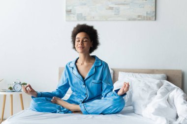 Pijamalı Afro-Amerikan kadın yatakta meditasyon yapıyor.