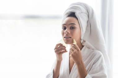 young african american woman in white towel massaging face with jade face scrapers clipart