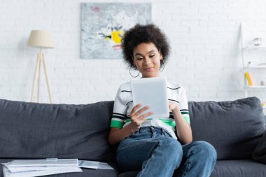 Genç Afrikalı Amerikalı kadın kanepeye otururken dijital tablet kullanıyor. 