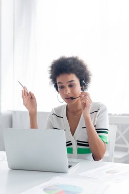Kulaklık takmış Afro-Amerikalı bir kadın laptopuyla evde video görüşmesi yapıyor. 